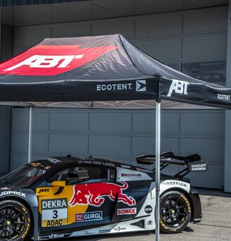 Vor einem Garagentor steht ein getuntes und bedrucktes Rennauto unter einem bedruckten Ecotent Faltpavillion Serie E1 der Größe 4,5 x 3 Meter.